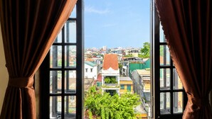 An open window with curtains, offering a view of a densely built urban area with various buildings and greenery. - Collection O Queen Hotel Central Hue (Hue)