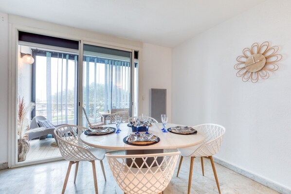 A dining area with a round table, white chairs, and a view through a sliding glass door. - bellevue apartment – on the port terrace and wifi (La Grande-Motte)