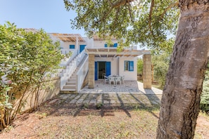 A two-story building with a white exterior and blue shutters, a stone staircase, and a patio area with a table and chairs.