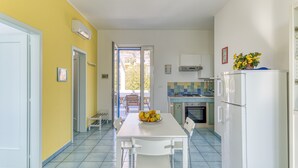Une cuisine équipée d’une table à manger, de chaises, d’un réfrigérateur et d’une fenêtre donnant sur l’extérieur.
