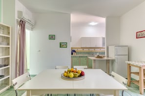 A dining area with a table, chairs, a fruit bowl, and a kitchen in the background.