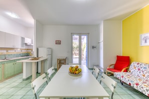 A dining area with a table, chairs, a fruit bowl, and a sofa.
