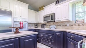 Una cocina con gabinetes superiores blancos, gabinetes inferiores oscuros, un microondas y un refrigerador de acero inoxidable.
