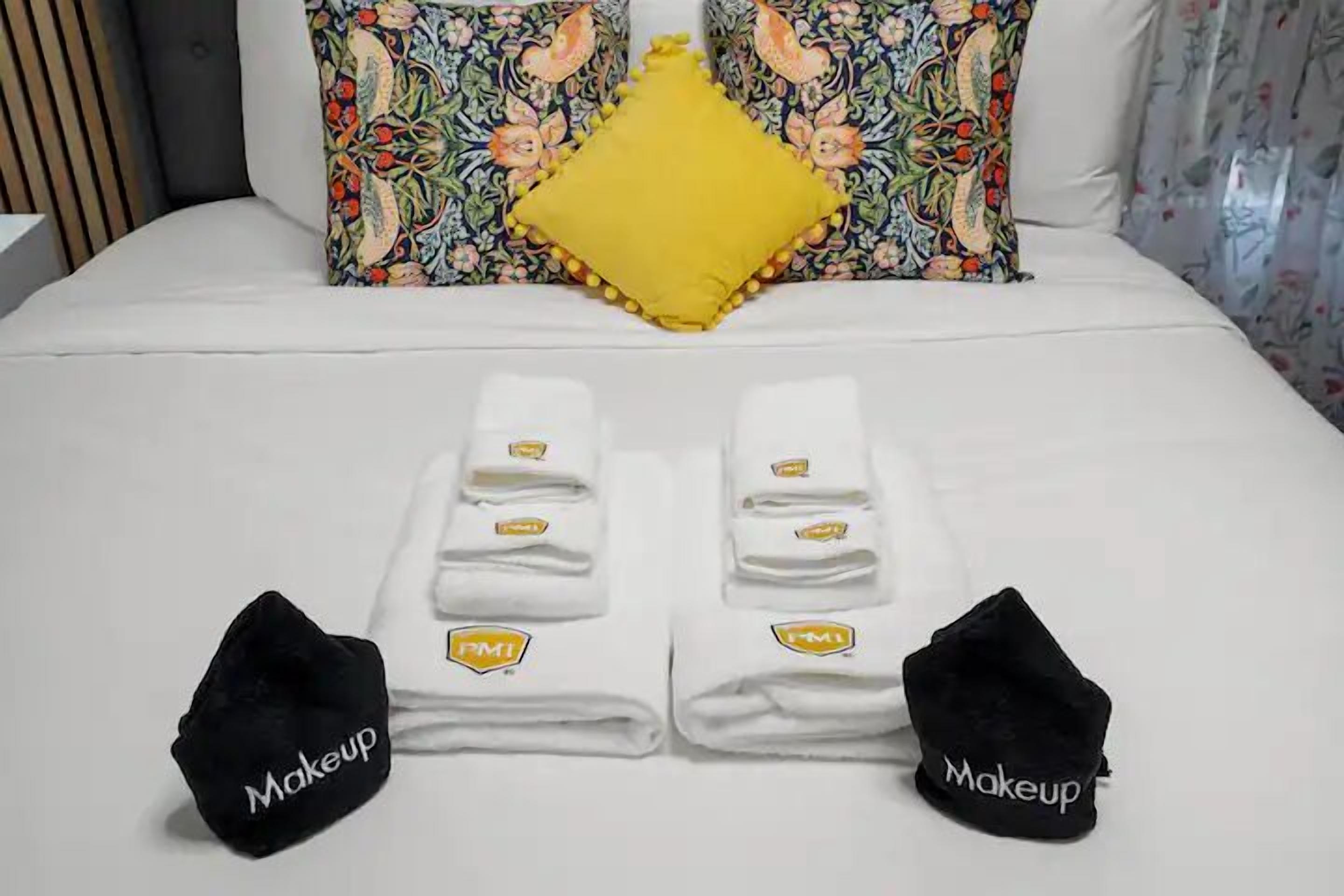A neatly made bed with two folded towels and two black bags labeled "Makeup" on either side.