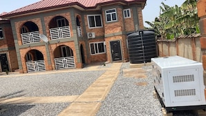 A multi-story building with a brick facade, multiple balconies, and a large water tank. - Cozy Bricks Apartment (Obomeng)