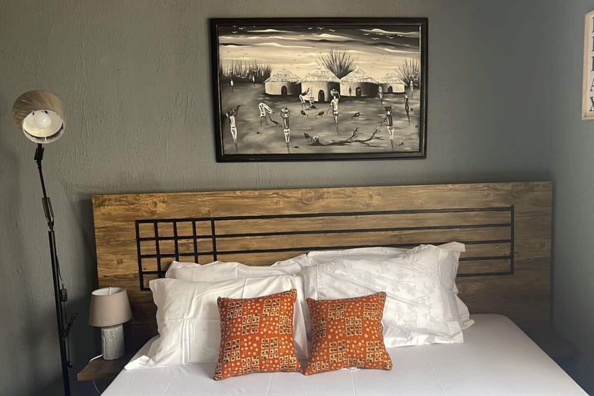 A bedroom with a wooden headboard, white bedding, and two patterned pillows.