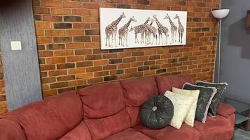 A red sofa with decorative pillows and a giraffe-themed wall art in a room with a brick wall.