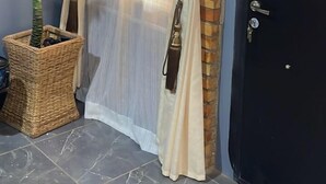 A room with a black door, a potted plant, a wicker basket, and a curtain. - Cozy Bricks Apartment (Obomeng)