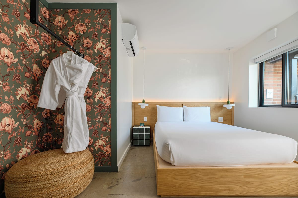 A bedroom with a wooden bed, a bedside table, a wall-mounted air conditioner, and a window with a view.