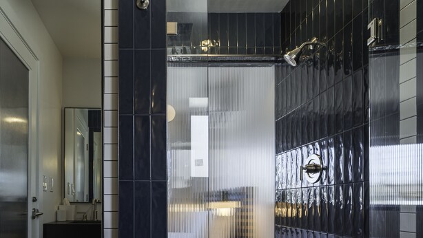 A modern bathroom with dark tiles, a glass shower enclosure, and a visible toilet. - Best Bet Motor Lodge  (Reno)