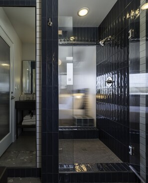 Un baño moderno con baldosas oscuras, cabina de ducha de vidrio y un inodoro a la vista.
