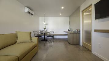 A compact living space with a sofa, a dining area with chairs, a small kitchen, and a TV mounted on the wall.