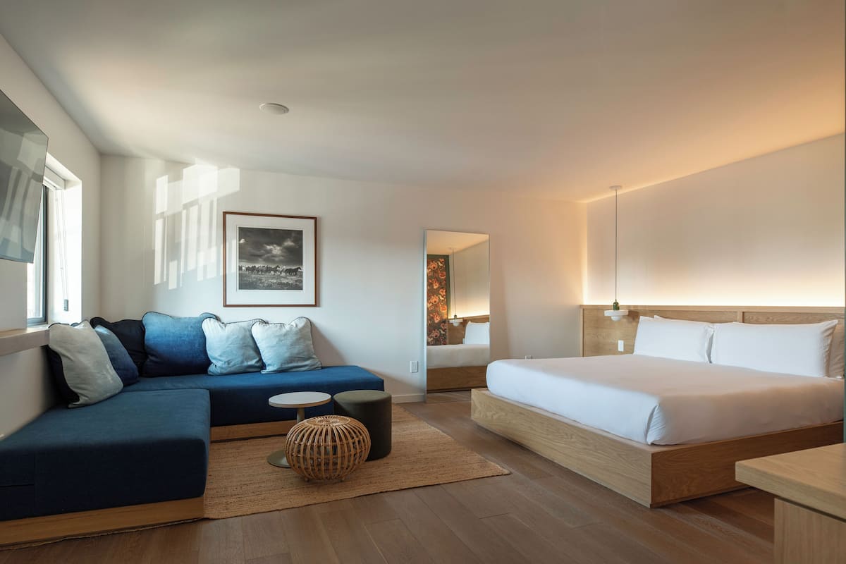 A modern hotel room with a large bed, a sofa, a small table, and a mirror.