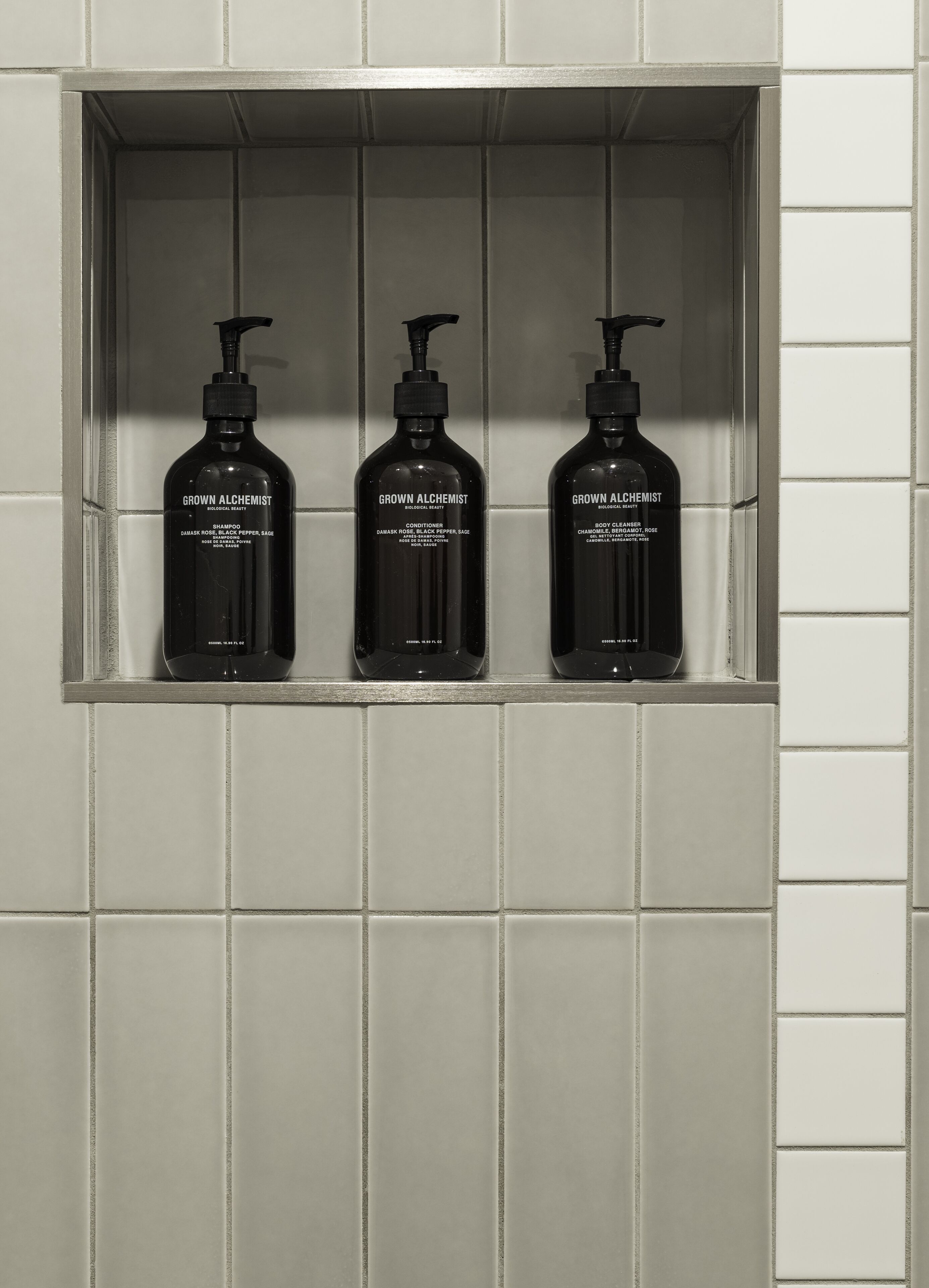Tres botellas negras de productos 'Grown Alchemist' en un estante empotrado en una pared de azulejos.
