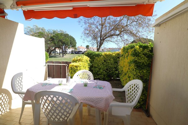 Un patio al aire libre con mesa y sillas, un espacio cubierto y vista a un barrio residencial.