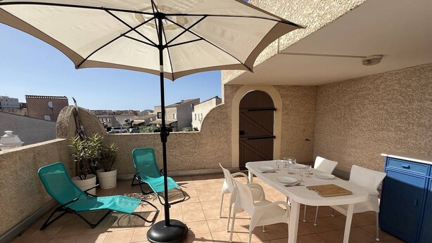 Una terrazza sul tetto con un tavolo apparecchiato per mangiare, sedie, un ombrellone grande e un armadietto blu.