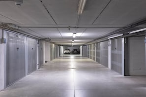 A long, narrow hallway with metal lockers on both sides and a few cars parked at the end.