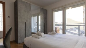 A modern hotel room with a large bed, a built-in wardrobe, and large windows offering a city view.