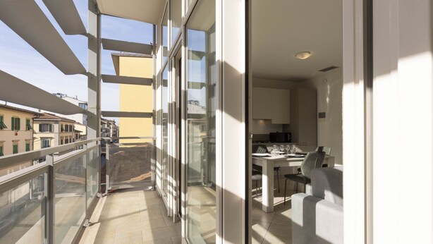 A modern apartment with a balcony, large windows, and a kitchen area.