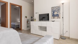 Un dormitorio moderno con una cama grande, un televisor sobre un mueble blanco y un cuadro en la pared.