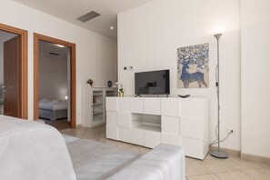 Ett modernt sovrum med en stor säng, en tv på en vit tv-bänk och en tavla på väggen.