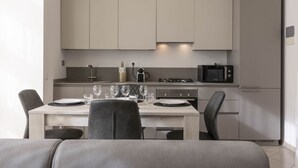 A modern kitchen with light-colored cabinets, a dining table set with plates and glasses, and a microwave on the countertop.