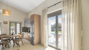 A modern kitchen with wooden cabinets, a stainless steel refrigerator, and a dining area with a round table and chairs. - Stone and Sea Villas (Lefkada)