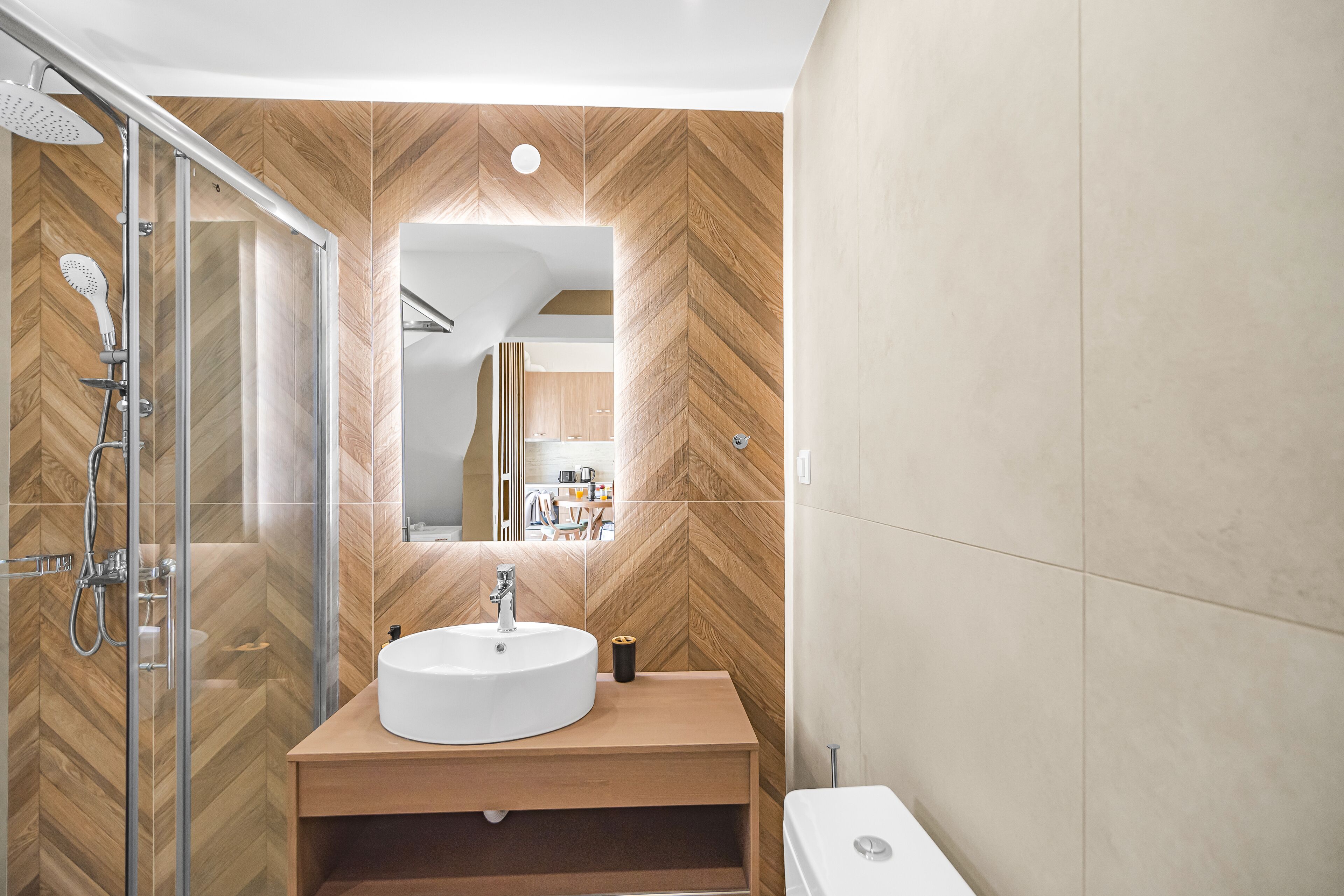 A modern bathroom with a wooden herringbone wall pattern, a glass-enclosed shower, a white sink, and a toilet.
