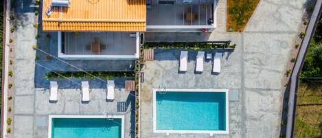 An aerial view of a resort with multiple swimming pools, sun loungers, and a wooden deck area.