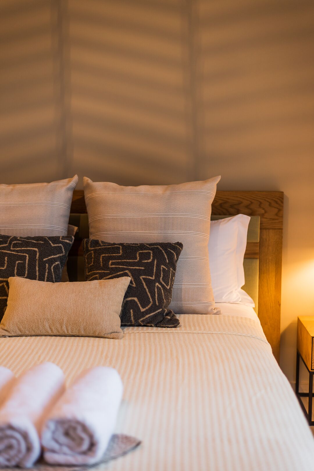A neatly made bed with patterned pillows and rolled towels.
