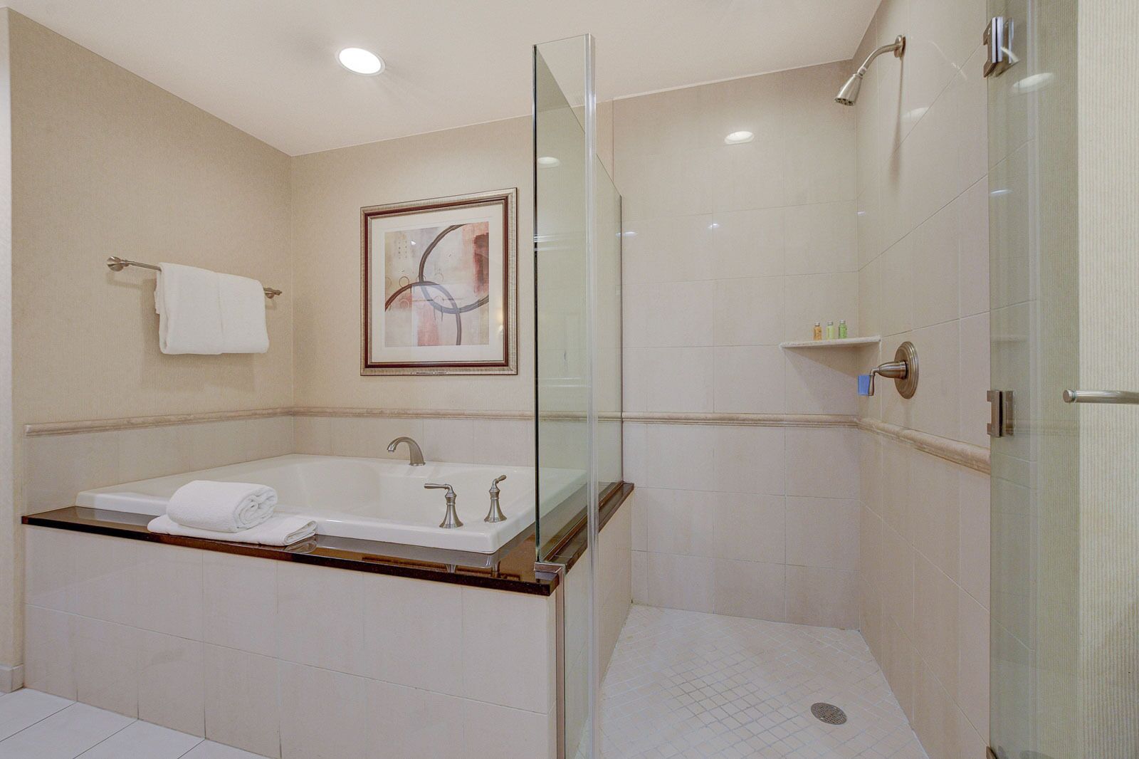 Ein modernes Badezimmer mit einer Glaskabine zur Dusche, einer großzügigen Badewanne und einem gerahmten Kunstwerk an der Wand.