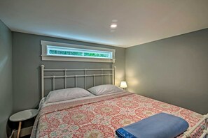 A bedroom with a bed, a bedside table, a lamp, and a window with blinds.