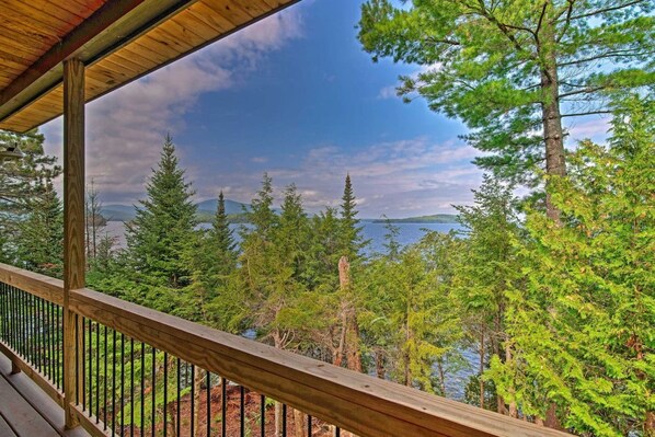 A wooden deck with a railing overlooking a forested area and a body of water.