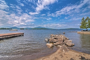 A calm lake with a wooden dock extending into the water, surrounded by rocks and a clear sky.