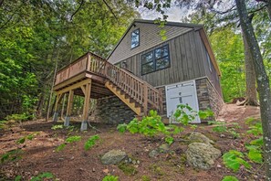 A cabin with a wooden deck and stone foundation, surrounded by a forest.