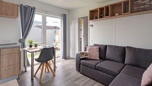 A modern living room with a grey sofa, wooden cabinets, and a dining area with a table and chairs. - Tiny Haus Central by Interhome (Beilngries)