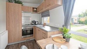 A compact kitchen with wooden cabinets, a built-in oven, and a window overlooking a garden. - Tiny Haus Central by Interhome (Beilngries)