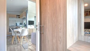 Una cuina moderna amb armaris de fusta, una zona de menjador amb caires blancs i un televisor visible.