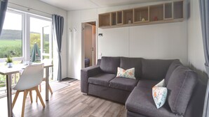 Un saló modern amb un sofà gris, una taula de dinar amb cadires i vista a l'exterior.