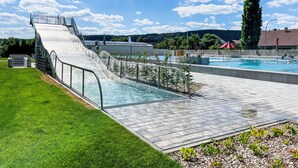 Una piscina amb tobogan, envoltada d'una zona verda i un cel serè.