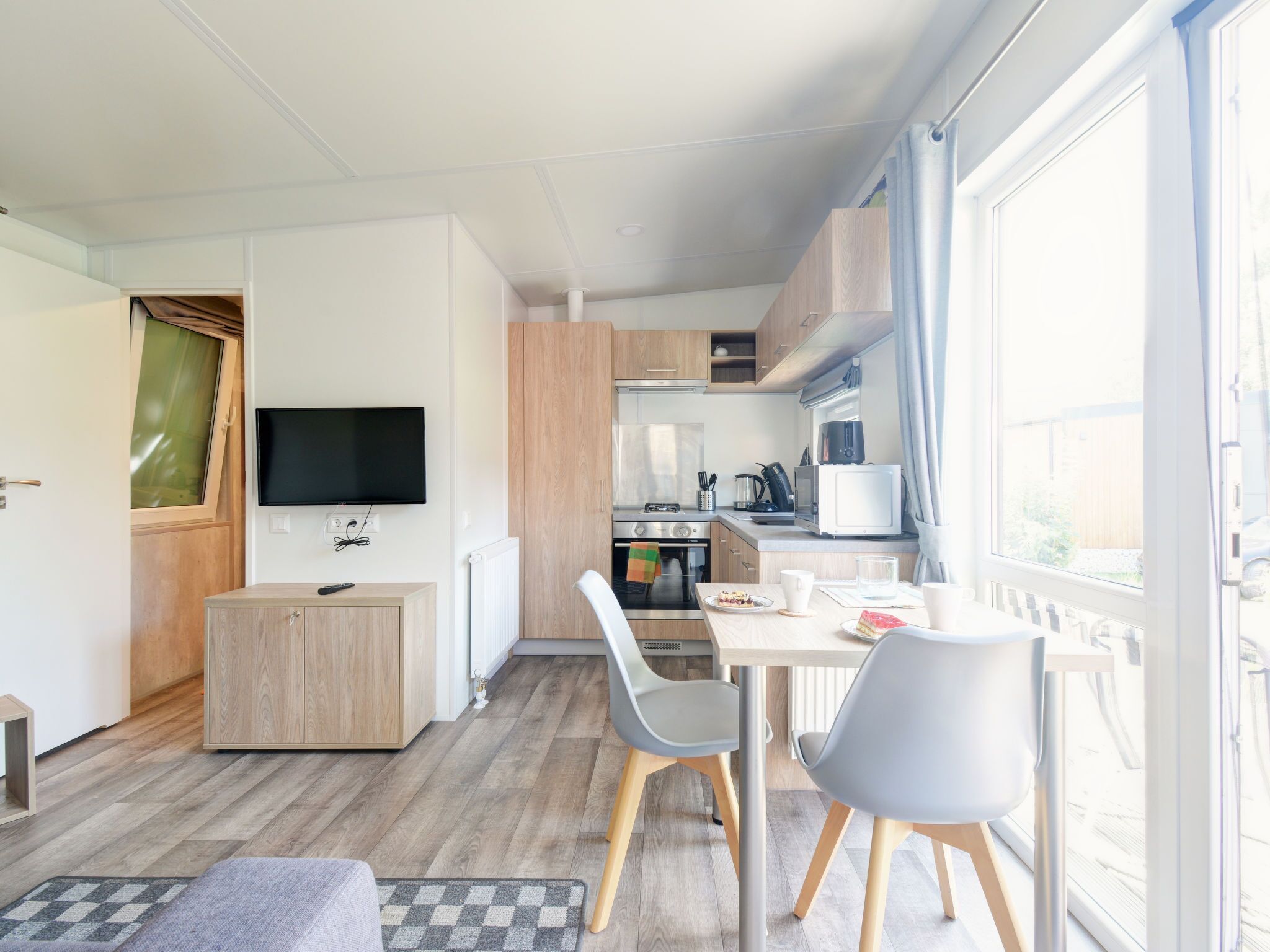 A modern kitchen with a dining area, a TV, and a window with a view.