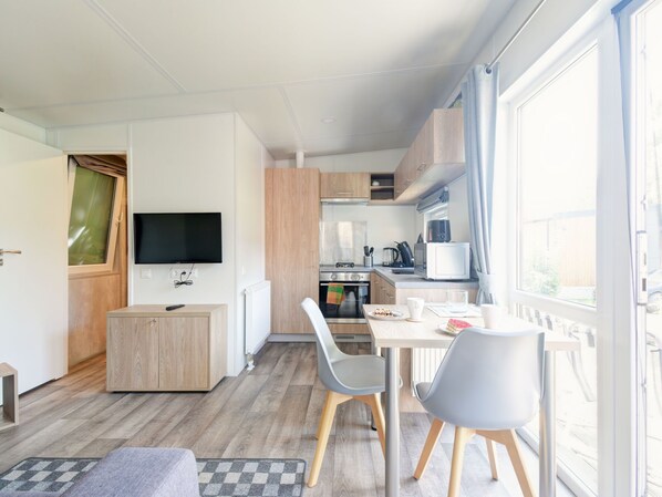 A modern kitchen with a dining area, a TV, and a window with a view.