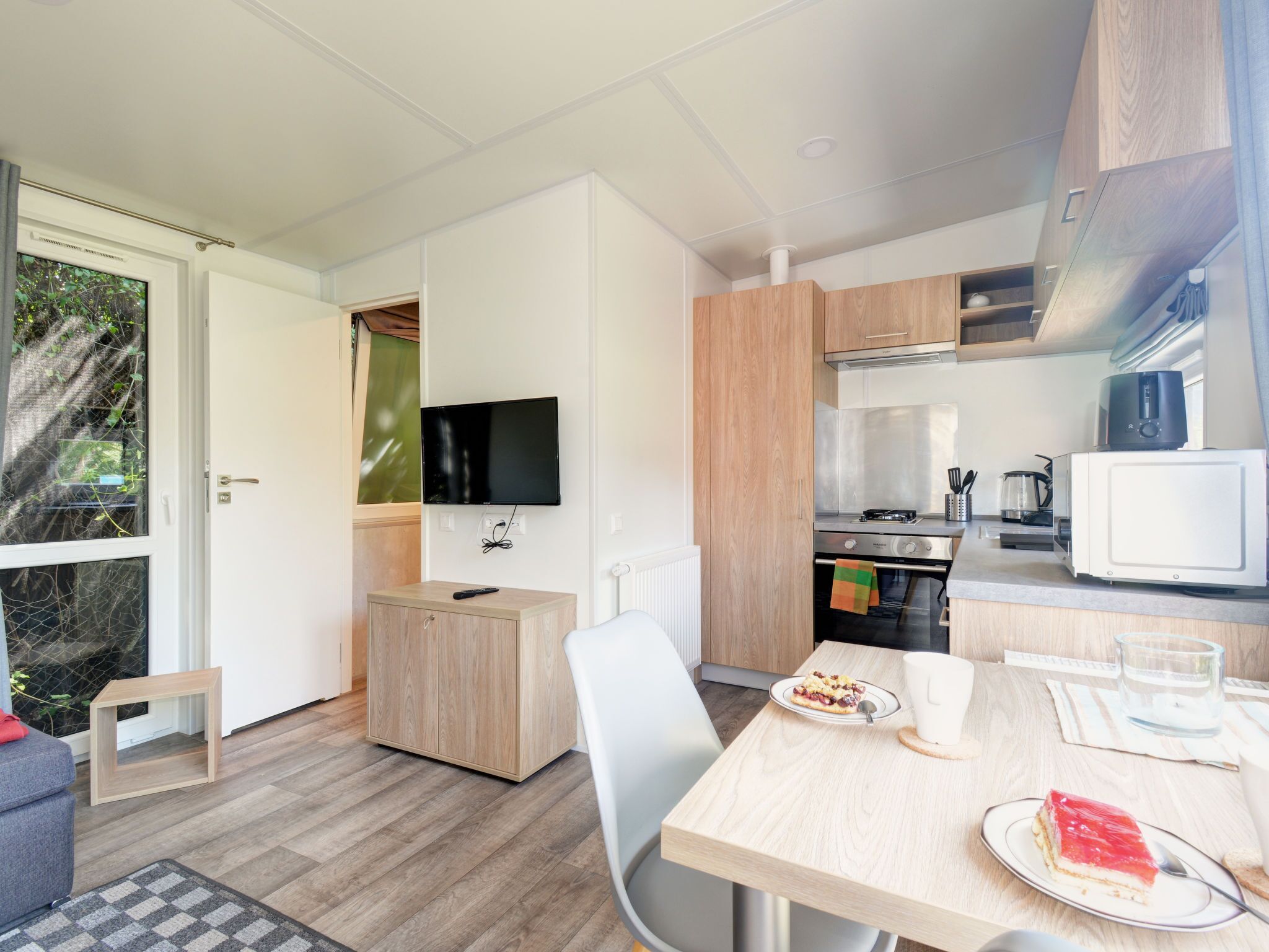 Une cuisine compacte avec un coin repas, un téléviseur fixé au mur et un petit coin salon comprenant un canapé et un fauteuil.