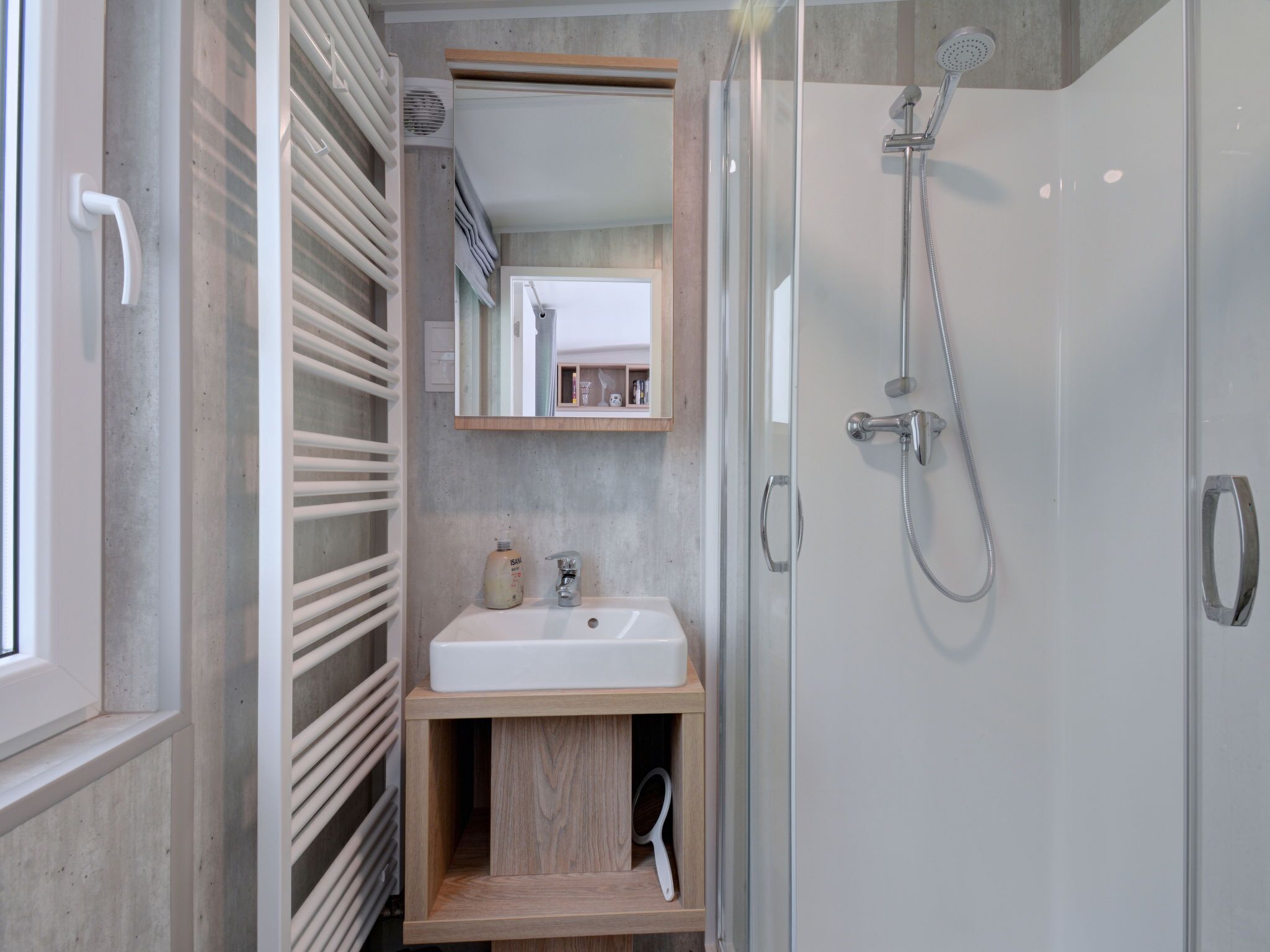 Un baño moderno con ducha envuelta en vidrio, un lavamanos blanco y un mueble de tocador de madera.