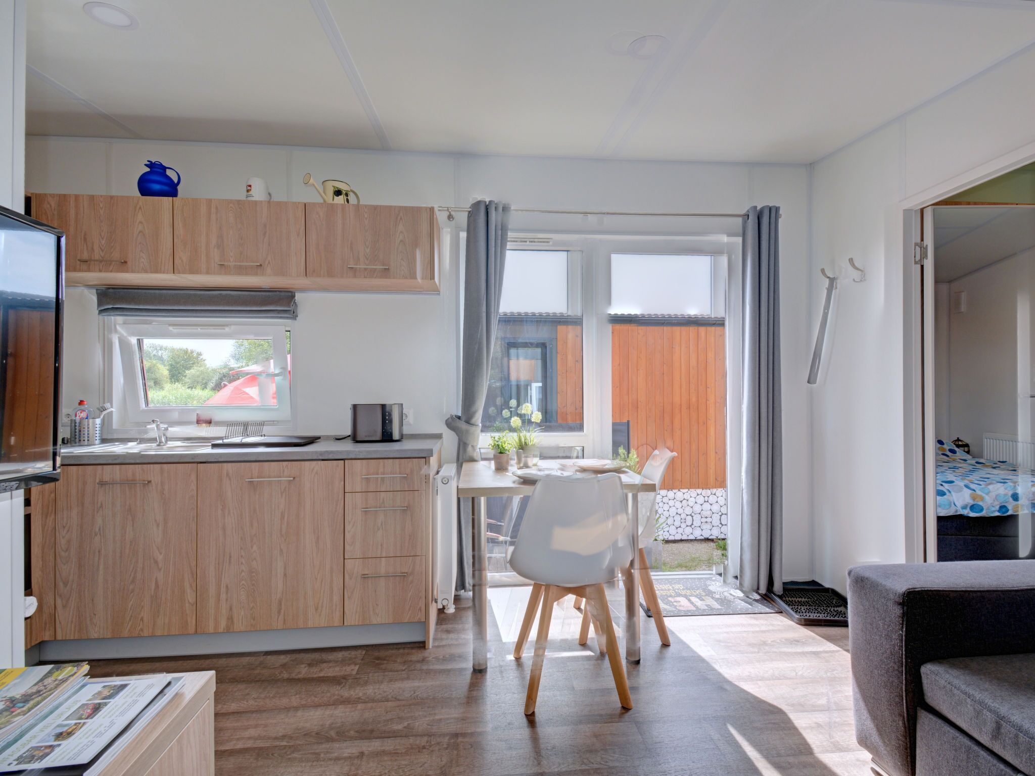 Una cucina compatta con mobili in legno, un'area pranzo con tavolo e sedie, e vista sull'esterno tramite ampie finestre.