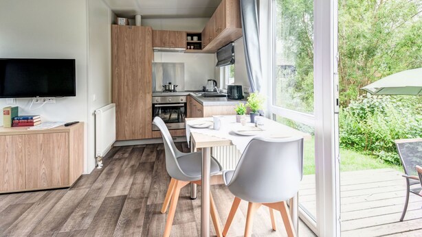 Una cocina moderna con armarios de madera, una mesa de comedor con sillas y un gran ventanal con vistas a la vegetación.