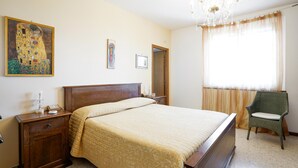 Un dormitorio con una cama grande, una mesita de noche de madera, una silla verde, una araña y un cuadro en la pared.