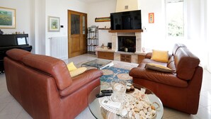 Una sala de estar con dos sofás de cuero marrón, una mesa de centro de vidrio con controles remotos, una chimenea y un televisor encima.