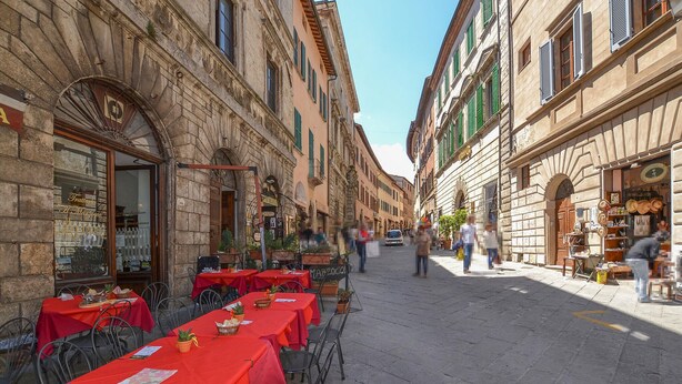 Calle con terrazas al aire libre, edificios de piedra y cielo despejado.