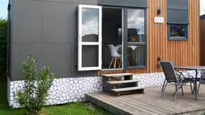 Ein modernes Haus mit grauer Fassade, einer Holzterrasse und einem Essbereich mit Gartenmöbeln.